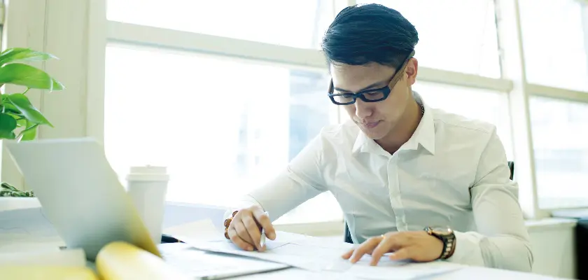 Young professional man in glasses working at a desk with documents and a laptop